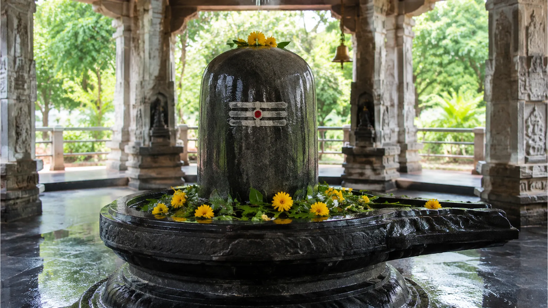 large stone shiva lingam inside temple with flowers and water