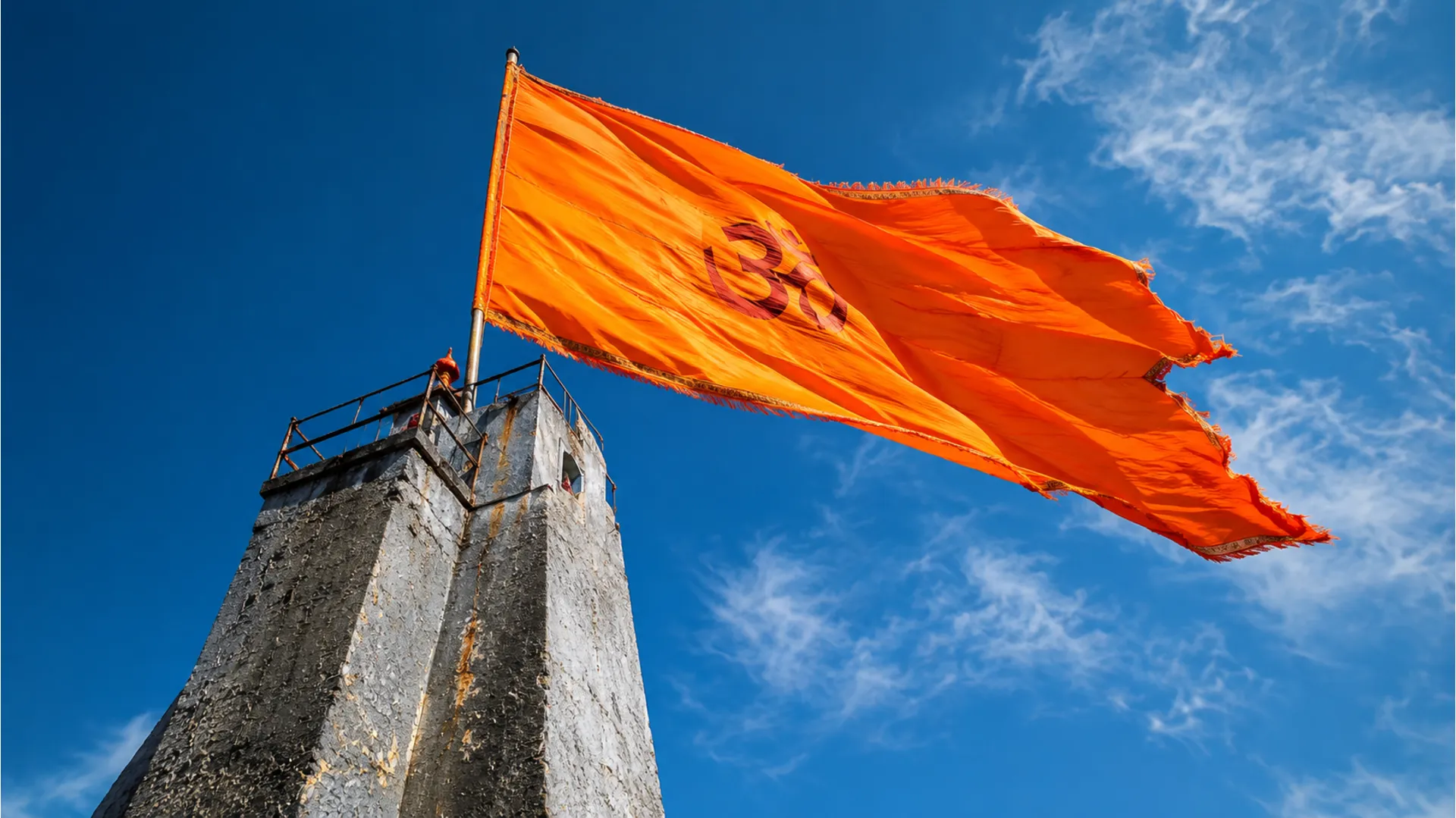A large saffron flag flying high on the main pillar of Nishkalank Mahadev Temple against a blue sky.