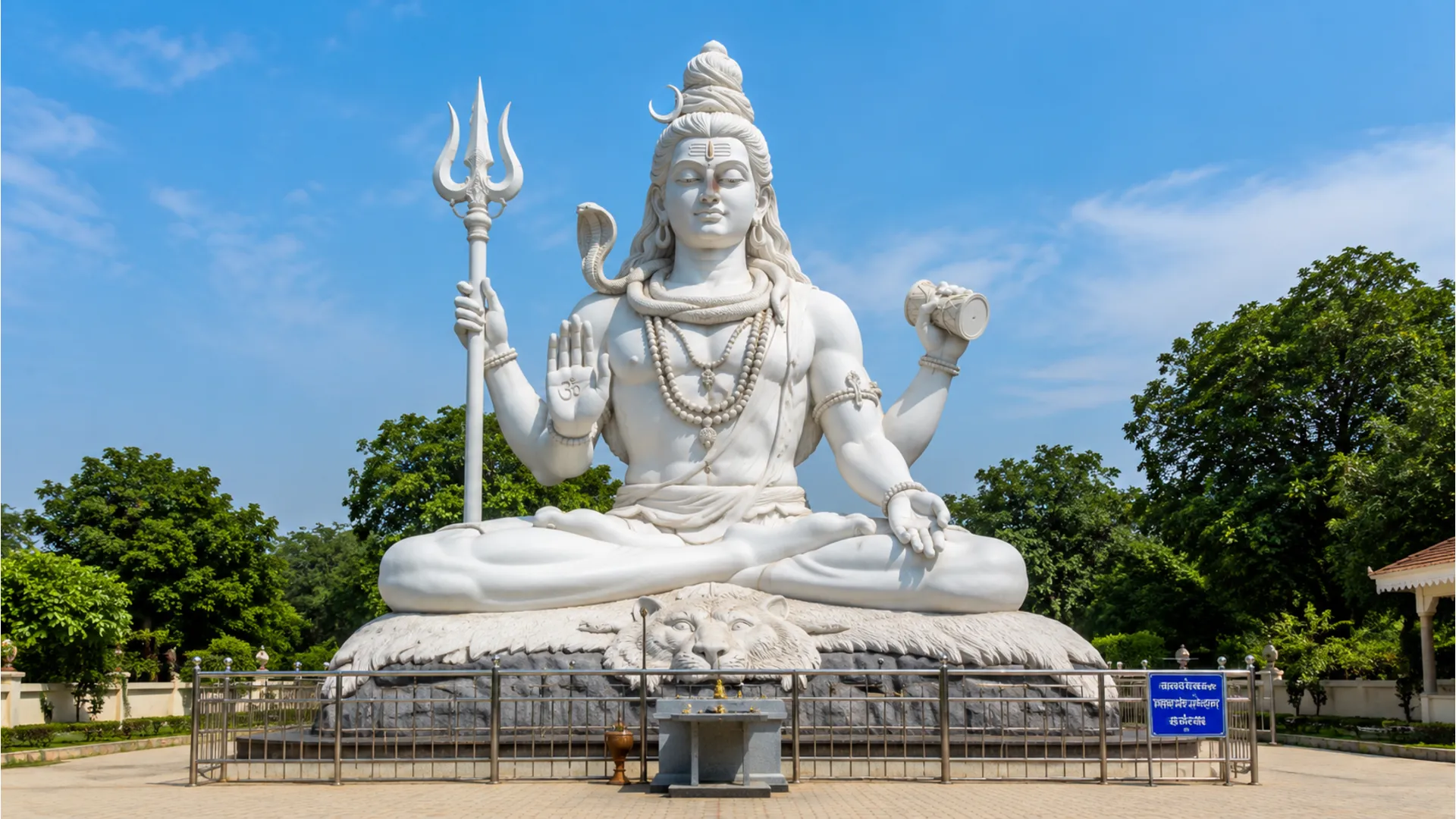 Large white Shiva statue holding a trident and drum in an outdoor temple area