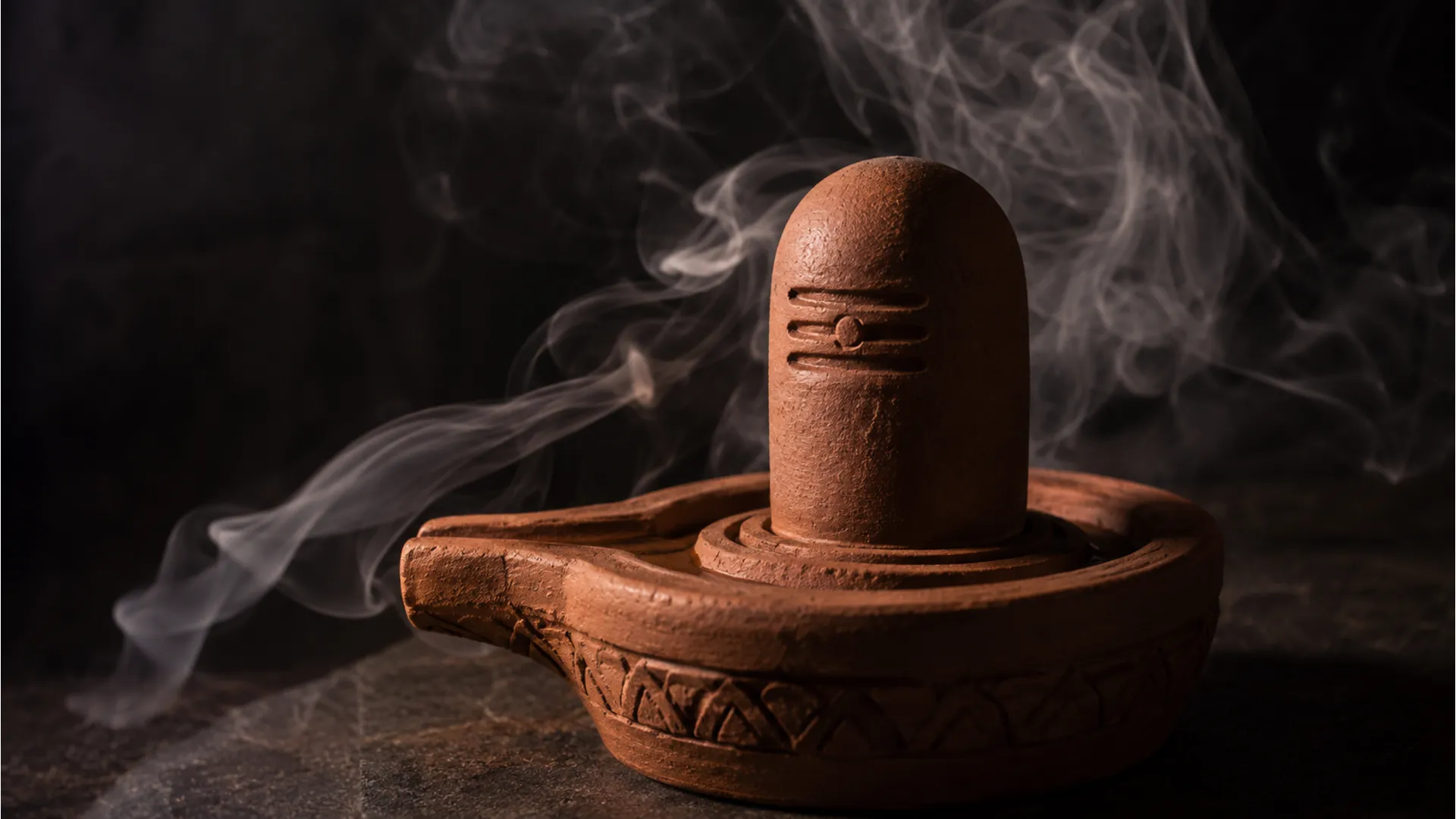 Handcrafted terracotta clay Shivling surrounded by soft incense smoke.