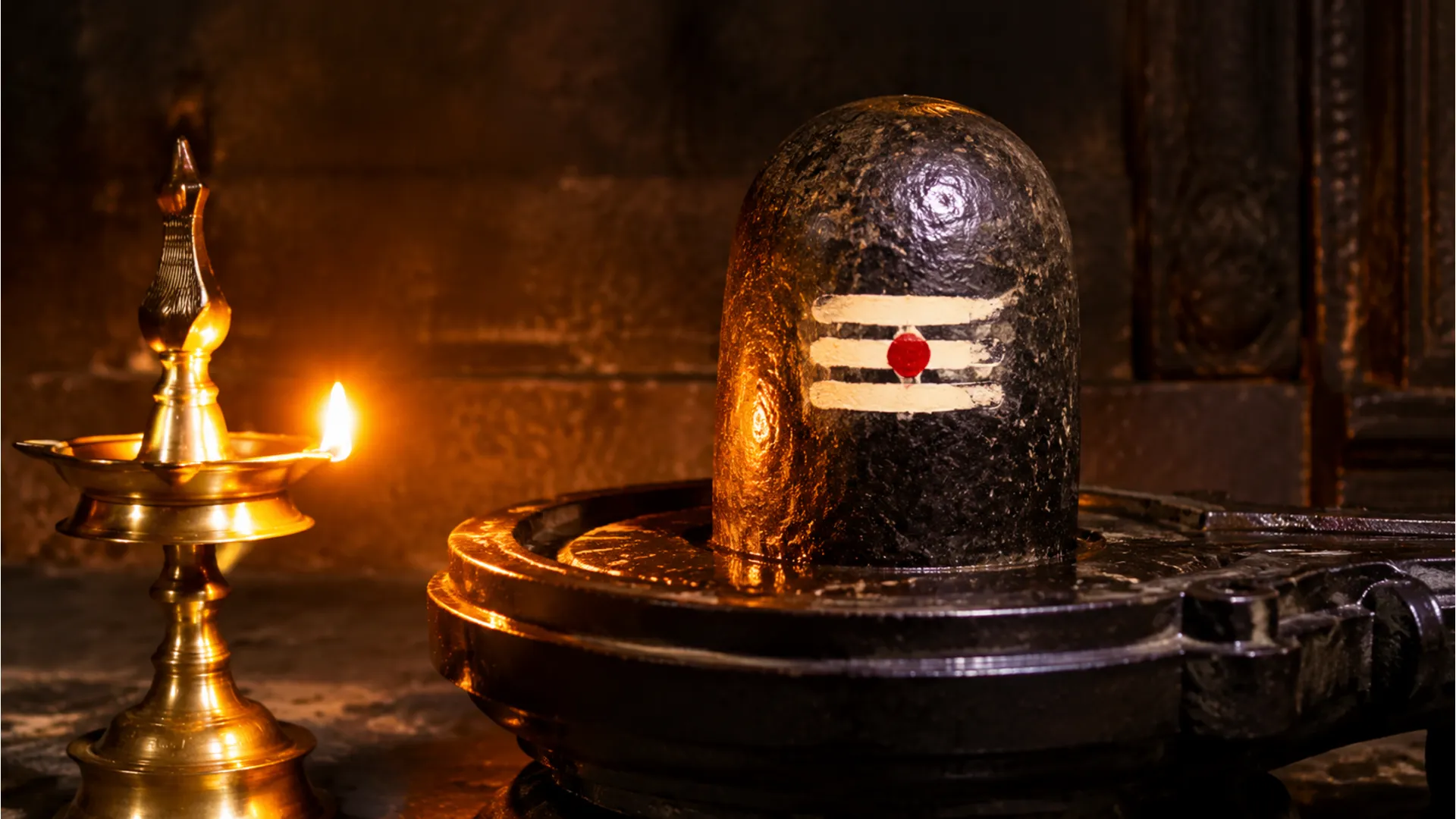 Black stone image shivling glowing in the warm light of a brass oil lamp