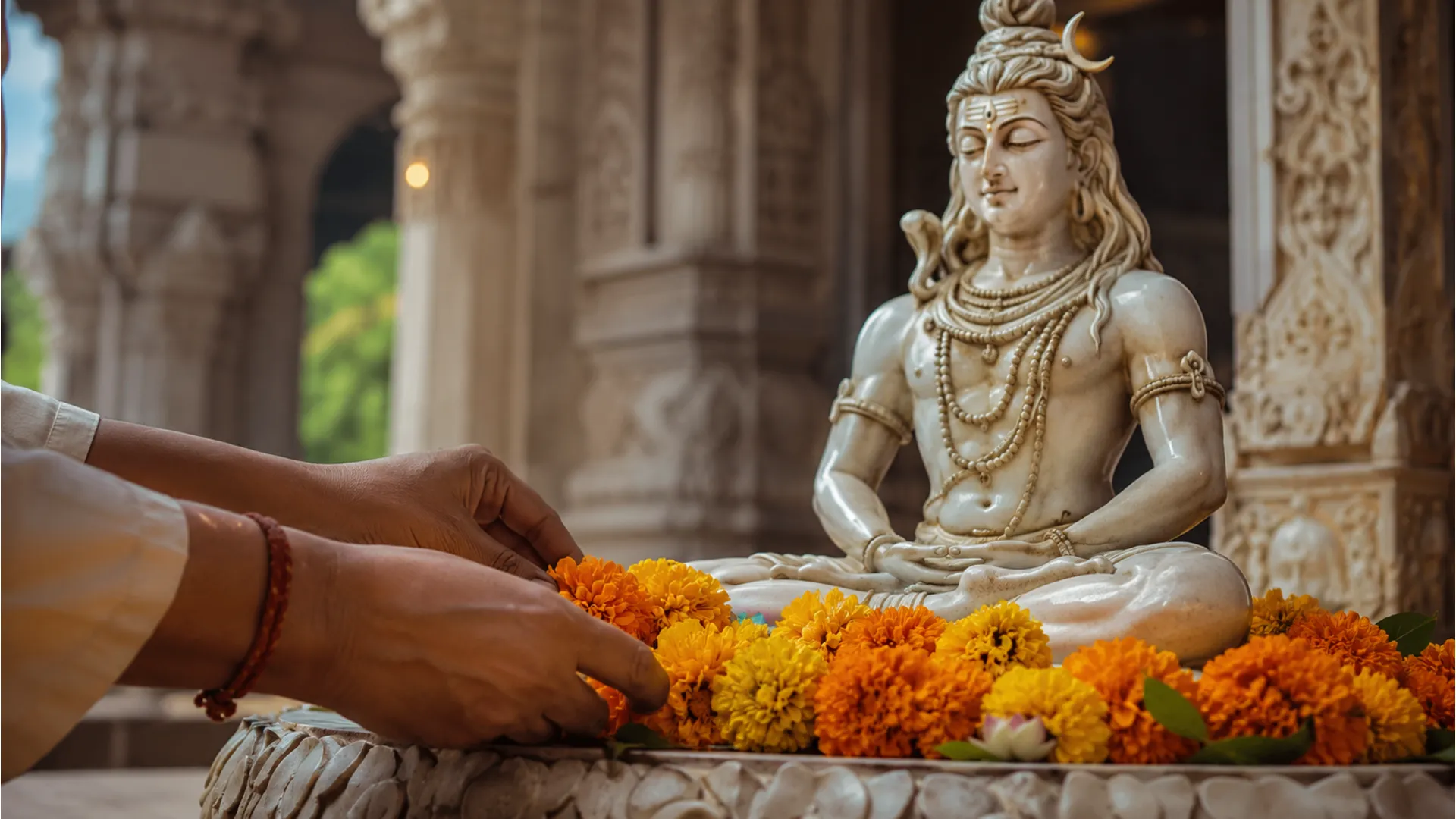 Hands of a devotee placing fresh marigold flowers at the feet of a meditating Lord Shiva statue