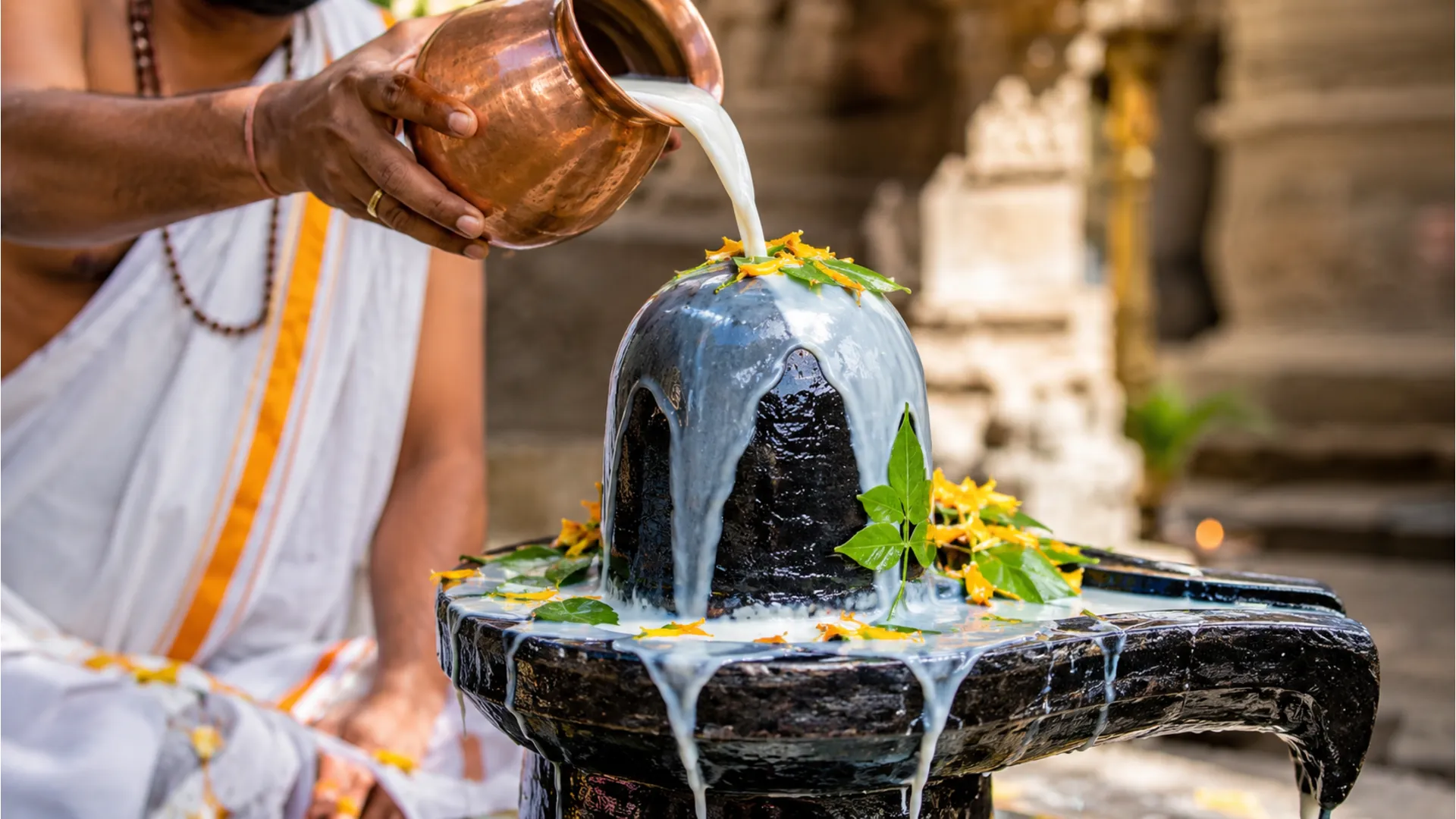 Fresh white milk pouring smoothly over a dark stone Shivling during a traditional temple ritual.