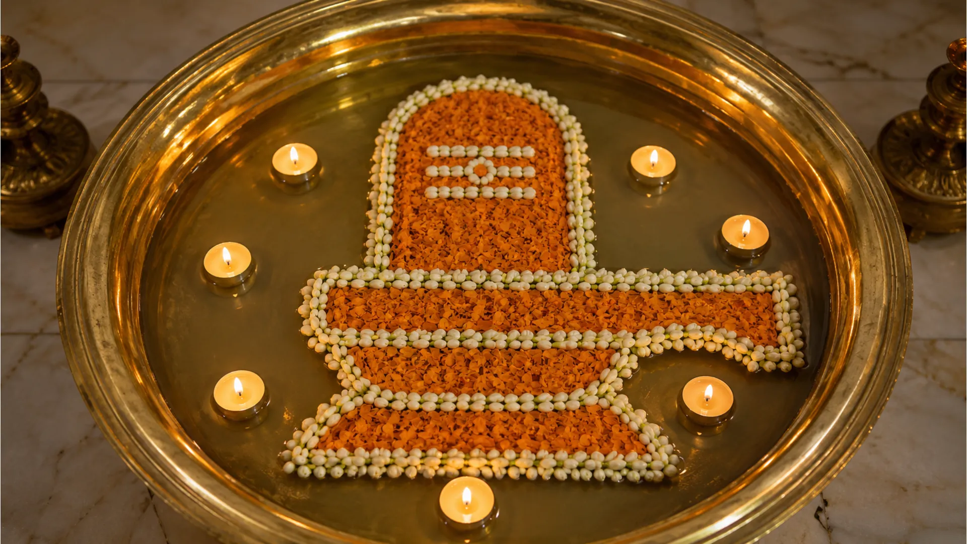 Full HD top-view of a floating rangoli in a large brass bowl depicting a Shivling shape using marigolds and floating candles.