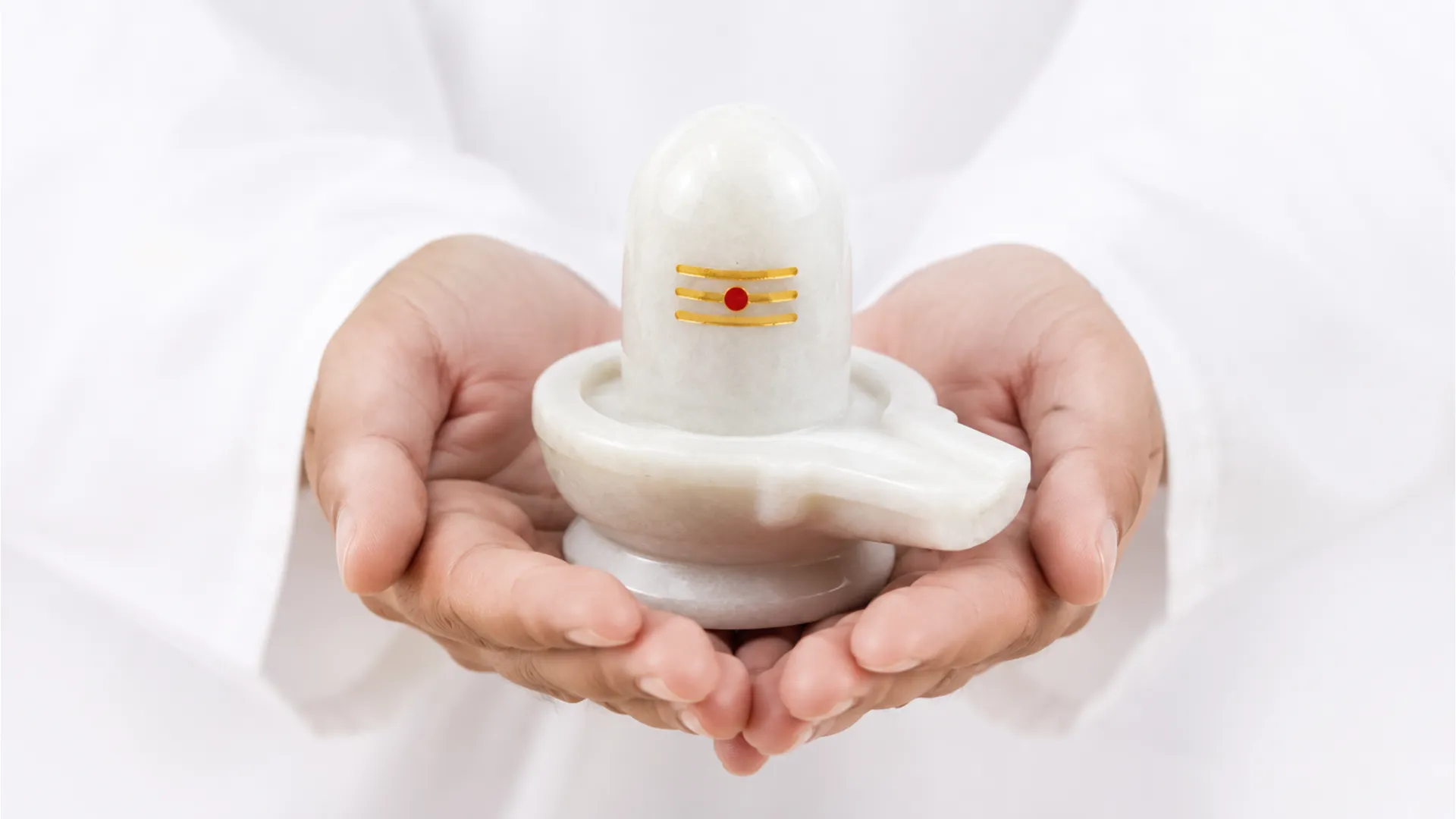 A pristine white marble Shivling held in hands with a yellow chandan tilak on it